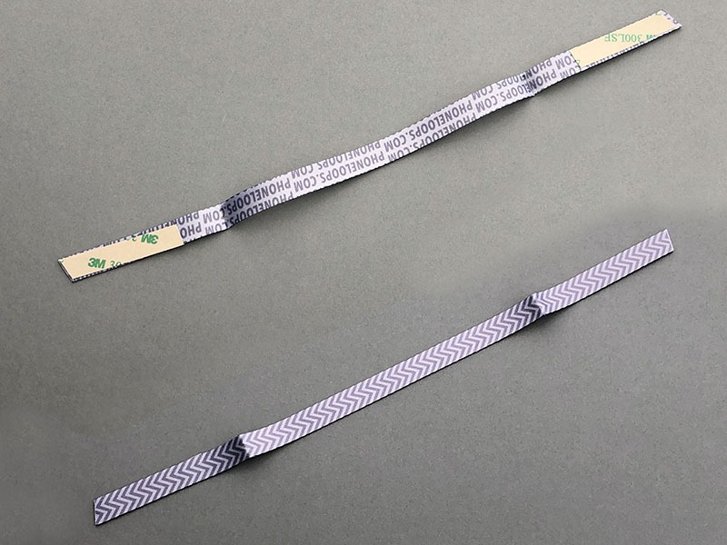 PHONE LOOPSの「NINJA LOOP」。これもリボンのような薄い化繊テープに両面テープが付いているもの。保護ジャケット側に貼り付け、指や手を通せるベルト状にして使うストラップです。直販価格は$4.99 USD​。