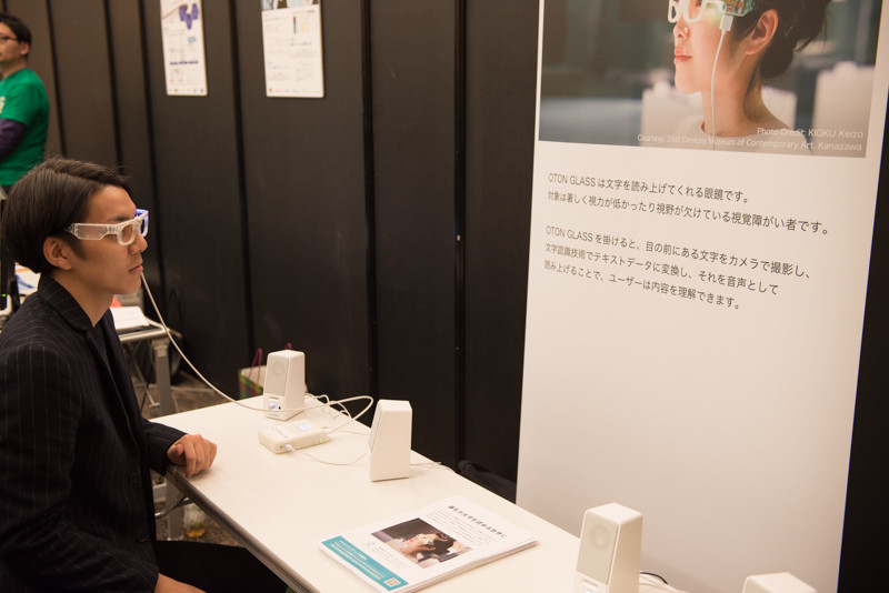 視覚障害者向けの読み上げ装置「OTON GLASS」、メガネ型デバイスに搭載されたカメラで文字を撮影、クラウド経由で文字認識を行い、音声読み上げを行う。翻訳して読み上げることも可能