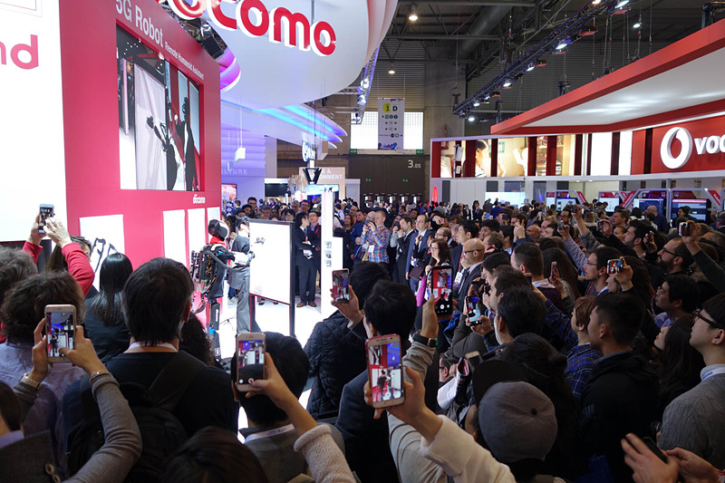 デモ中のドコモブース前。Vodafoneブースとのあいだの通路は埋め尽くされんばかりの人だかりができる