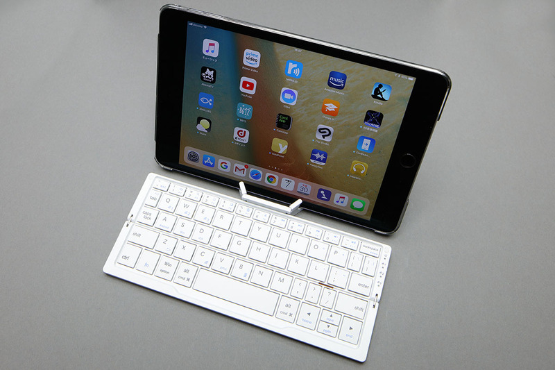 左はiPhone X、右はiPad miniを乗せた様子。スタンドにかかる重さが大きいほど、スタンド下部の滑り止めが机面に強く当たり、キーボードが滑りにくくなり安定します。ただ、iPhone Xなどの軽めの端末を乗せた状態でも、机面が滑りにくい材質なら実用上問題はないことが多いです。ちなみに、スタンドには10.5インチiPad Proなど大きめの端末を乗せることもでき、スタンドの脚の開き方で端末の画面角度を調整できたりもします。