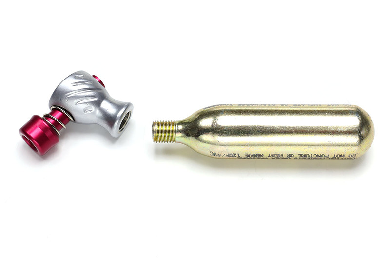 最もシンプルな類のCO2インフレーター。この製品の場合、ノズル部の下にCO2ボンベをネジ込み、その状態で赤いノズルをタイヤのバルブに強く押し当てると、ほぼ一瞬でタイヤに空気が入ります。コンパクトで軽いため、自転車での常時携行にもよく向きます。なお、CO2ボンベは使い捨てで、1本300円前後で売られています。