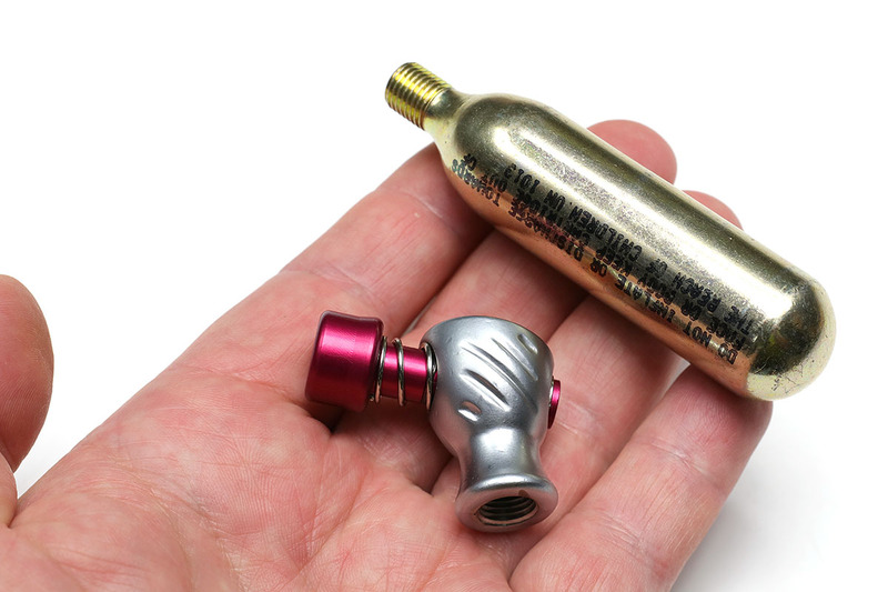 最もシンプルな類のCO2インフレーター。この製品の場合、ノズル部の下にCO2ボンベをネジ込み、その状態で赤いノズルをタイヤのバルブに強く押し当てると、ほぼ一瞬でタイヤに空気が入ります。コンパクトで軽いため、自転車での常時携行にもよく向きます。なお、CO2ボンベは使い捨てで、1本300円前後で売られています。