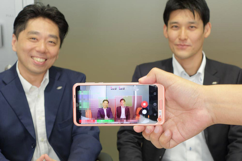 シャープの山本氏（左）と村上氏（右）。手前で動作してるのはAIエンジンのパラメータを表示する開発用アプリ。人物を認識し、笑顔などを数値化している