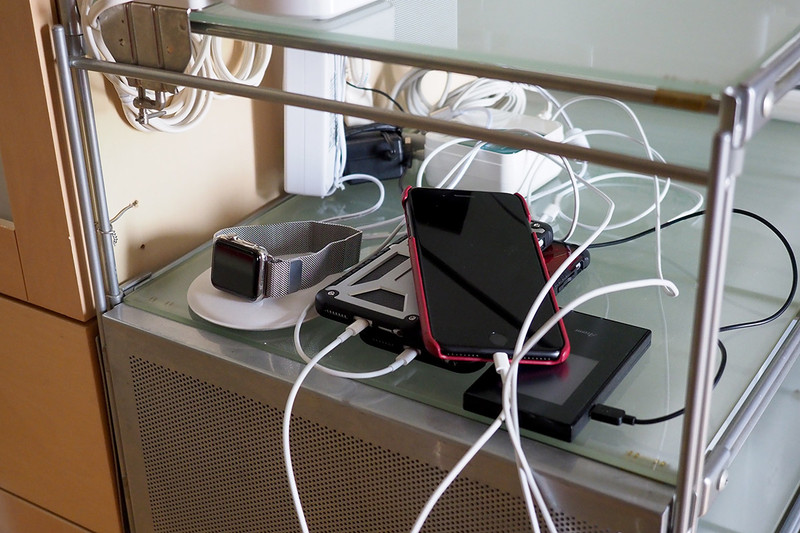 左写真は、単にUSB-ACアダプターと端末をつないで充電していた頃の様子（再現）。右写真は、ある充電スタンドを使って充電している様子。明らかに片付きますし、USBケーブルを短いものに交換すれば乱雑さ煩雑さも激減です！