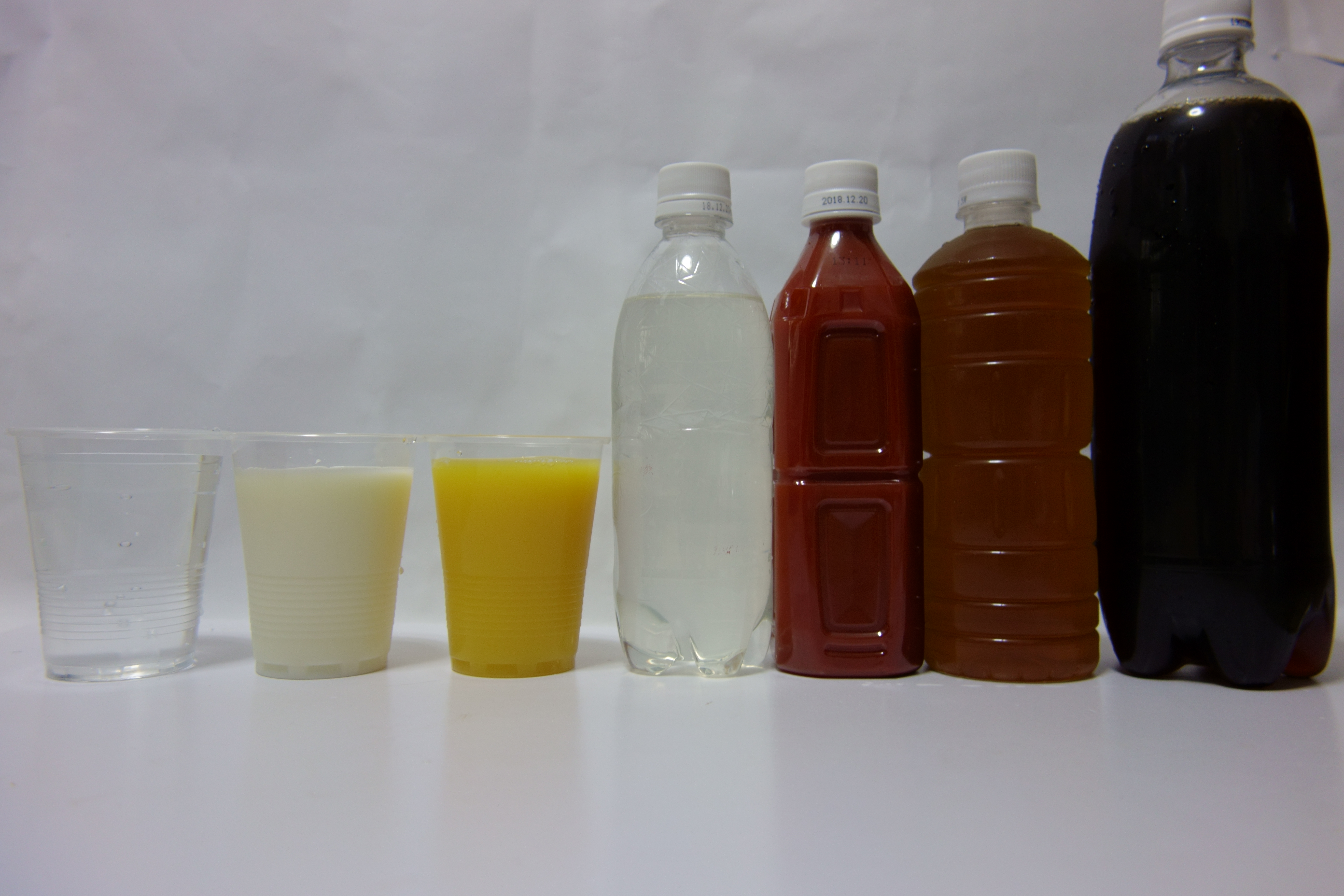 コンデジで撮影した飲み物。左から水道水、牛乳、オレンジジュース、スポーツ飲料、トマトジュース、ウーロン茶、コーラ