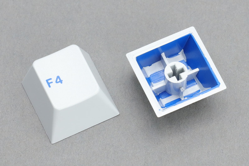 ダブルショットキーキャップの一例。それぞれ2色の樹脂を使ってつくられています。白＋青、グレー＋青ですが、これらキーキャップの場合は青がキートップ刻印となり、白やグレーがキーキャップ全体の色になっています。