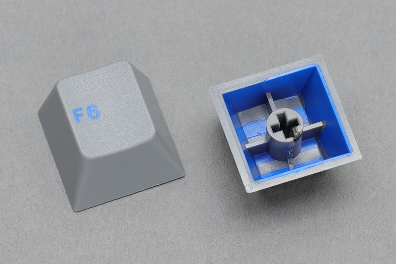 ダブルショットキーキャップの一例。それぞれ2色の樹脂を使ってつくられています。白＋青、グレー＋青ですが、これらキーキャップの場合は青がキートップ刻印となり、白やグレーがキーキャップ全体の色になっています。