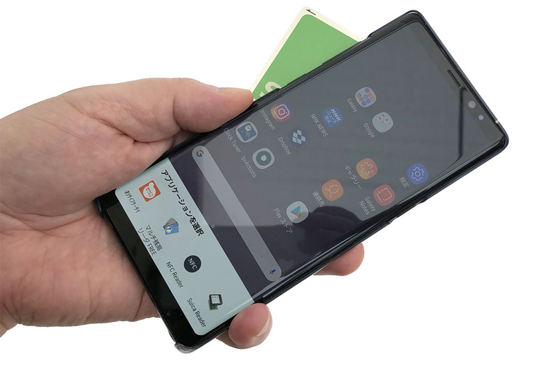 Android端末で使える電子マネーカードリーダー系アプリ（←多々存在します）をNFC対応端末にインストール。端末は筆者が使用中の「Galaxy Note8」（<a href="https://k-tai.watch.impress.co.jp/docs/column/stapa/1102189.html" class="strong bn" target="_blank">レビュー記事</a>）です。端末背面に電子マネーカードをかざすと……。