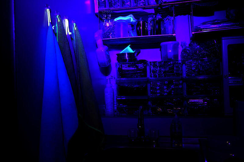 仕事場の流し台周辺。UVライトを当てたら、布巾を吊す黄色い紐、白いタオル、白い樹脂のブラシが顕著に光りました。蛍光染料を使って色鮮やかに見えるようにしている製品、という感じ。