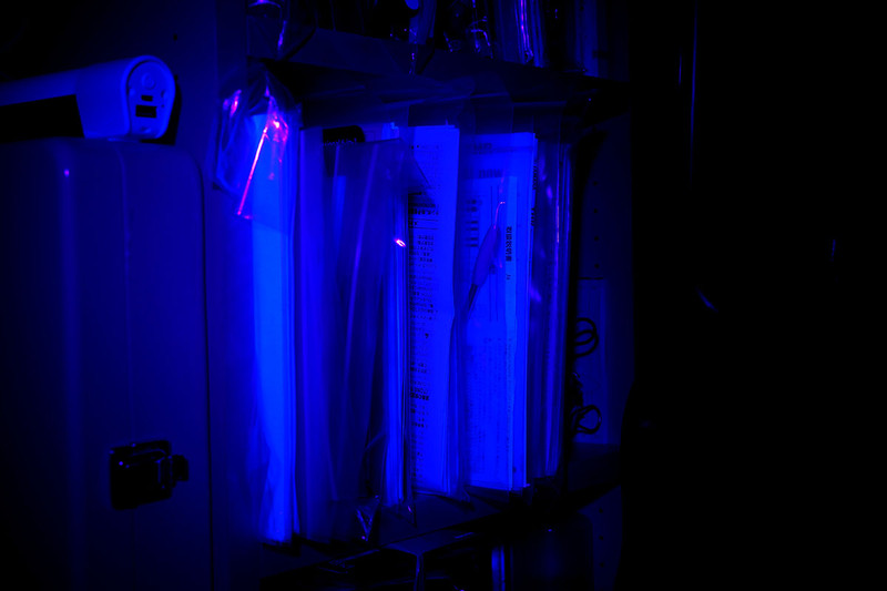 説明書の類が入った本棚を照射。説明書ってけっこう強めに光りますね～。紙質を抑えつつキレイな冊子に見えるように蛍光染料を多めに使っている？　よくわかりませんが興味深いです。