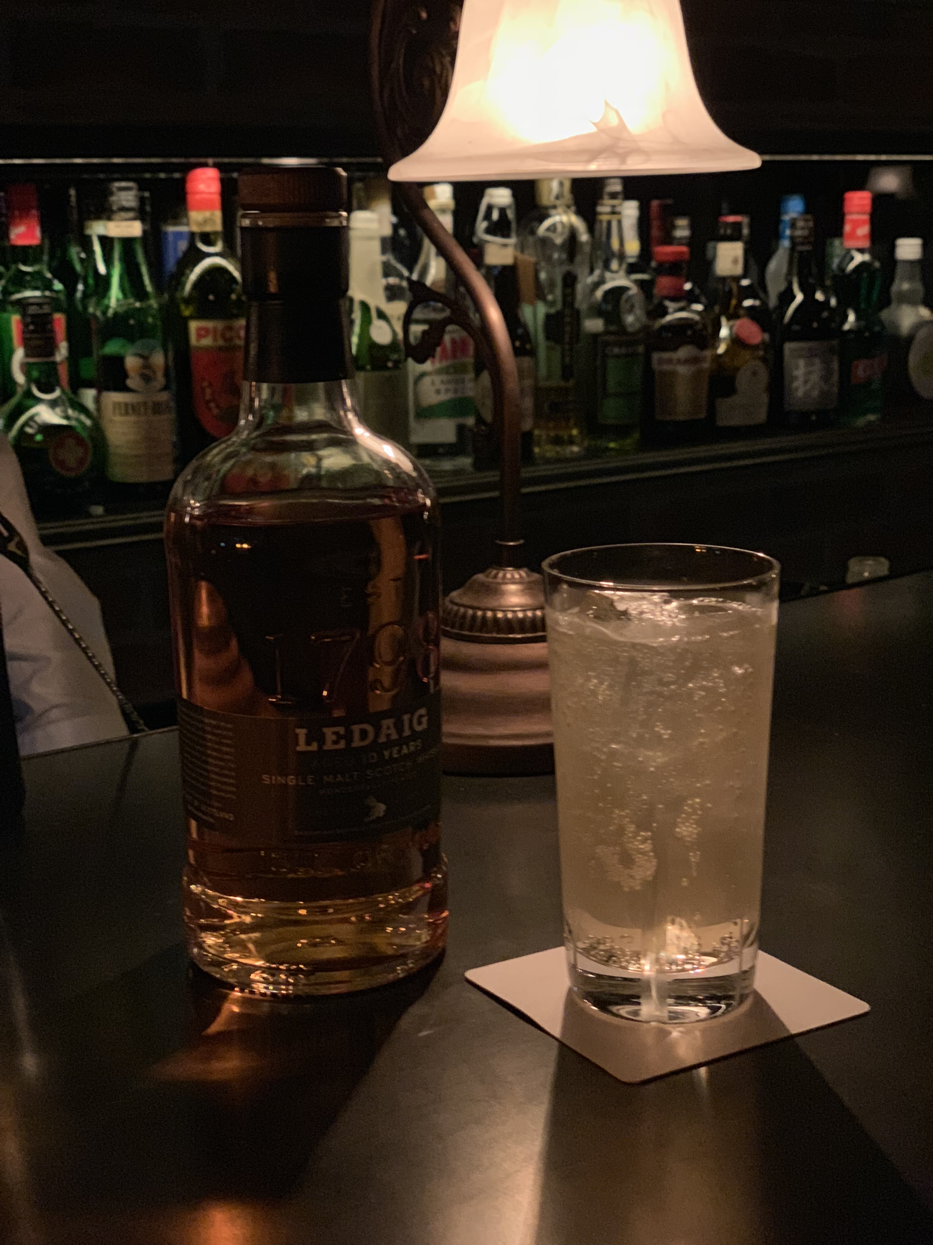 薄暗いバーで撮影。ボトルが並ぶ後ろの棚も明るく撮影できている　※リンク先は3024×4032ドットのオリジナル画像