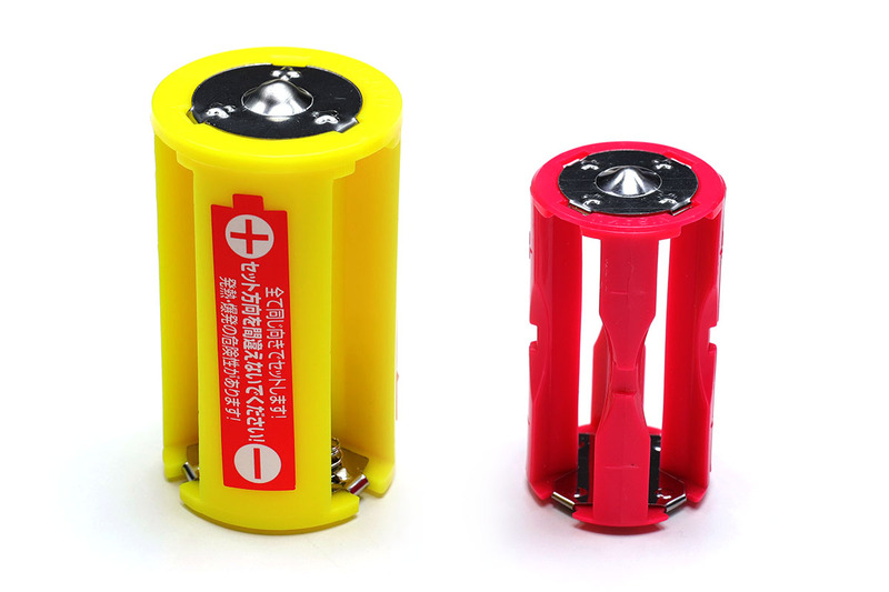 ニサクの「No.6001 単1サイズ AAx3>D」と「No.6010 単2サイズ AAAx4>C」。黄色いほうが単1タイプで、単3形電池×3本が単1形電池に化けます。ピンクのほうは単2タイプで、単4形電池×4本が単2形電池になります。それぞれ、複数の同型電池を並列でつないでいるので、電圧はそのまま（単1形電池や単2形電池とも同じ）。変換元の電池の本数が多いぶん、機器を使える時間が長くなります。どちらも3本セットで648円というショップが多いような感じ。