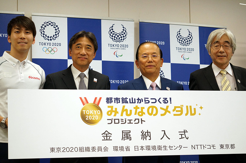 納入式の様子。左からリオパラリンピック銅メダリストの山田選手、NTTドコモの吉澤社長、武藤東京2020組織委員会事務総長、藤吉秀昭日本環境衛生センター副理事長