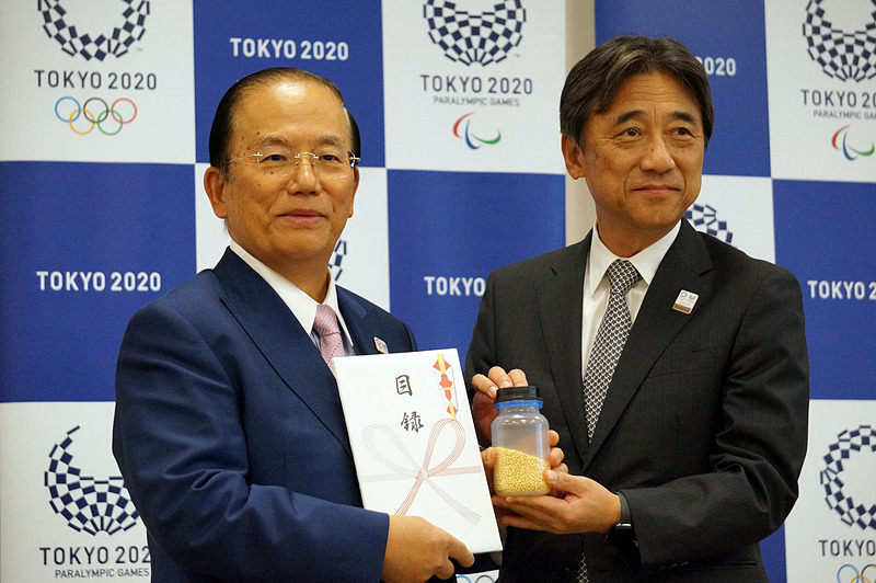 納入されたリサイクル金属の目録を手にする武藤事務局長（左）と、ドコモの吉澤社長（右）