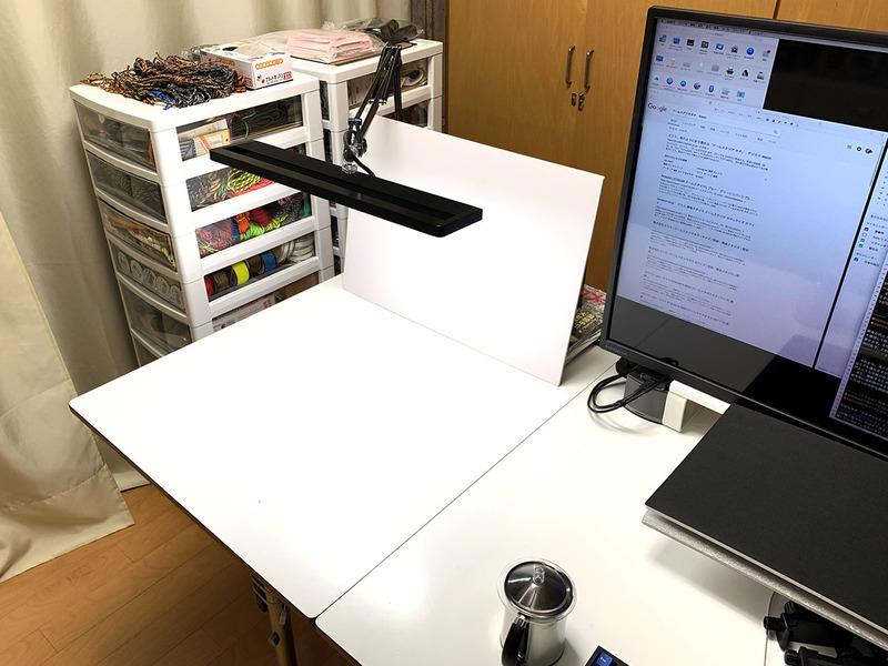 筆者の机上スタジオ。仕事用デスクトップPCの左側の僅かなスペースです。机面は白。背景を整理して後のレタッチなどを行いやすくするため、机面と同じような白いボードを後方に置きます。今回使う主な光源は白色LEDのデスクライト×1灯。天井には蛍光灯の照明や白色LEDの照明があり、これらもある程度被写体を照らしています。