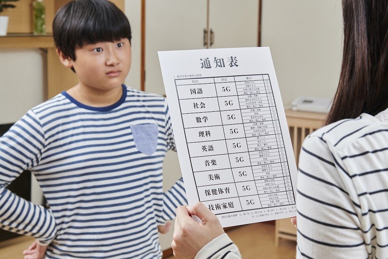 「5Gと書かれた通信簿を誇らしげに見せる息子」