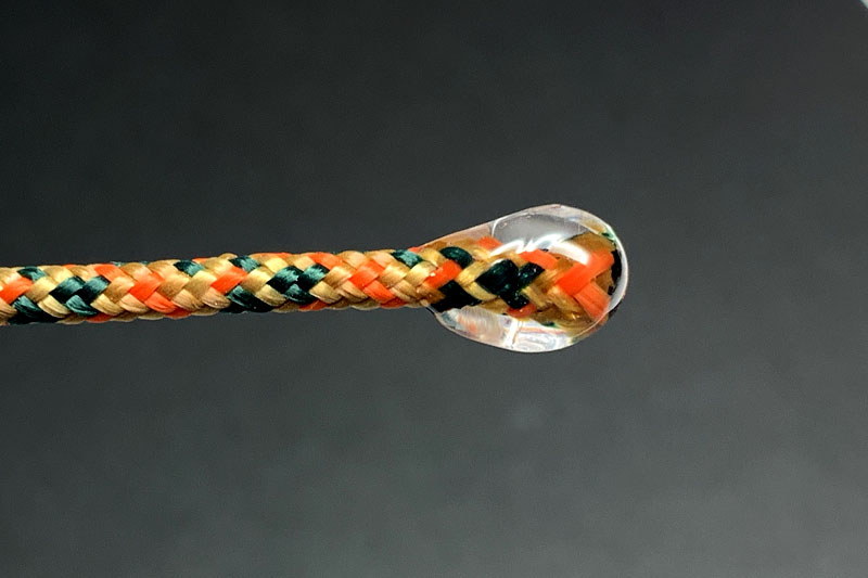 左は紐の先に紫外線硬化樹脂を付けて丸く固めたもの。ストッパーに通せば、紐の端を結ばなくてもストッパーから抜けません。紐と紫外線硬化樹脂は強固に癒着しますので、強度も十分。結び目がないぶん嵩張らず、紫外線硬化樹脂は透明なので見栄えもイイです。