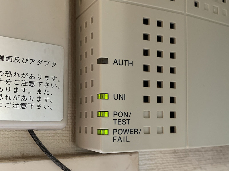 三菱電機製の「GE-PON〈M〉A GE-PON-ONU〈1〉〈2〉」というONUです。拙宅では窓の上の壁に取り付けてあります。ONU左下の4つのランプで動作状態がわかります。中央写真のように、4つのランプ全てが緑点灯（うちUNIランプは点灯もしくは点滅）の状態が正常。どれかのランプがオレンジや赤に点灯・点滅したり消灯したりし続けている場合、何らかのトラブルが起きています。右写真は拙宅の光回線ダウン状態のもの。AUTHランプが消灯したままですが、これは故障中か光回線運用準備中を示しています。