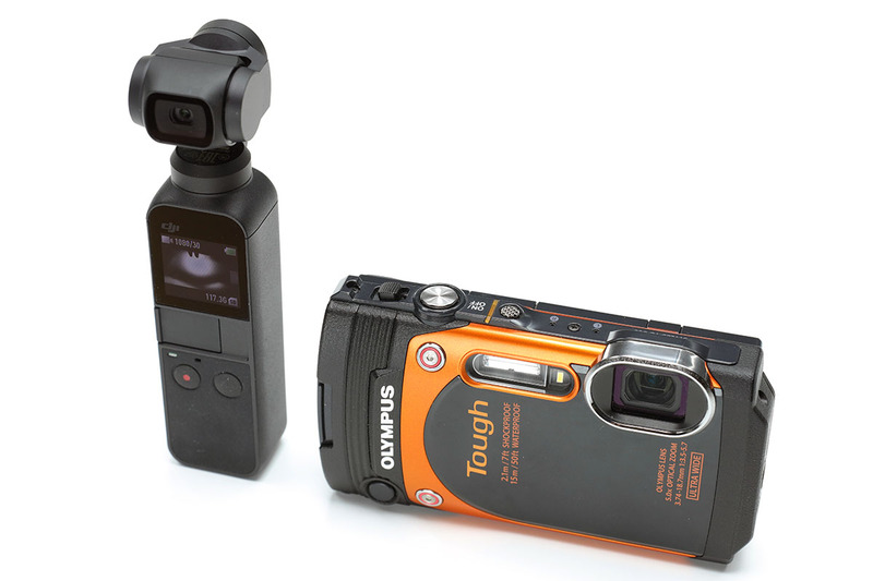 Osmo Pocketのサイズは高さ121.9×幅36.9×厚さ28.6mmで、質量は116g。上部がスタビライザー・カメラ部で、小さな液晶モニターと操作ボタンを備えます。オレンジ色のカメラはオリンパス「TG-860」（<a href="https://www.olympus-imaging.jp/product/compact/tg860/" class="strong bn" target="_blank">公式ページ</a>）で、わりと標準的なサイズのコンパクトデジカメ。Osmo Pocketこういったコンデジよりもさらにコンパクトなカメラです。