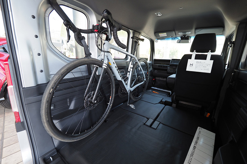 助手席を倒せば、後部とつながった状態のフルフラットになります。車体左側が大開口で、助手席～後部がフルフラットになりますので、自転車を左側からポンと載せられちゃう！　右写真は自転車を逆向きに載せて後部から見た様子。ロードバイクなら2台並べて載せられ、後部右側の座席に座ることもできます。