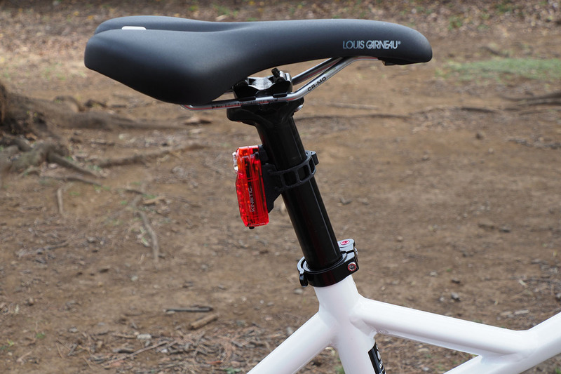 こちらはテールライトの「SYNC KINETIC」（<a href="https://www.cateye.com/jp/products/safety_lights/TL-NW100K/" class="strong bn" target="_blank">公式ページ</a>）。シートポスト（サドル下のパイプ）に装着していて、曇天下の点灯イメージです。後方から見ると鋭いような赤色光がよく目立つライトです。なお、このライトは走行からの減速時に赤く明るく光ります（キネティックモード）。ブレーキランプ的に使えるというわけです。