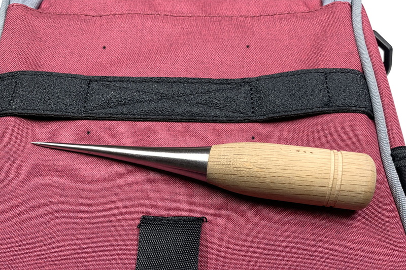 穴を開ける方法は「尖った金属製の道具を熱して突き刺す」というもの。ナイロン製などのバッグだと、この方法で手軽にキレイな穴が開き、ホツレなども出ません。写真の道具は「目打ち」とか「クジリ」とよばれるものです。これをバーナーやライターの炎で加熱し、バッグの印の部分にプスリと。