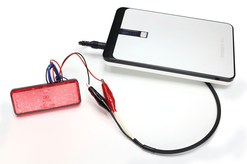 バッテリーのDCジャックから12Vを取り出せるケーブルを作ってみました。先端はワニ口（わにくち）クリップで、これを12V対応モジュールにつないでテストなどします。赤く光っているのは12V対応のテールランプで、12Vの電圧をかけるだけで点灯します。……でも不意にワニ口クリップの先端がショートしたら激ヤバな予感。使用には非常に気を使います。