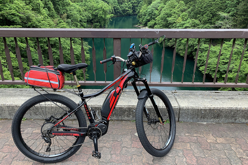 愛用中のe-bike、ミヤタ「RIDGE-RUNNER」（<a href="https://k-tai.watch.impress.co.jp/docs/column/korekori/1186998.html" class="strong bn" target="_blank">関連記事</a>）。安楽化・便利化の方向でいろいろイジっていますが、このe-bikeでたびたび奥多摩方面を走っています。左は多摩川の上にかかる橋。右は奥多摩むかし道の途中です。東京都内ですが自然でいっぱいのエリア。青梅駅から奥多摩湖（小河内ダム）の往復がいつものコースで、距離は約55km、獲得標高は約600mです。