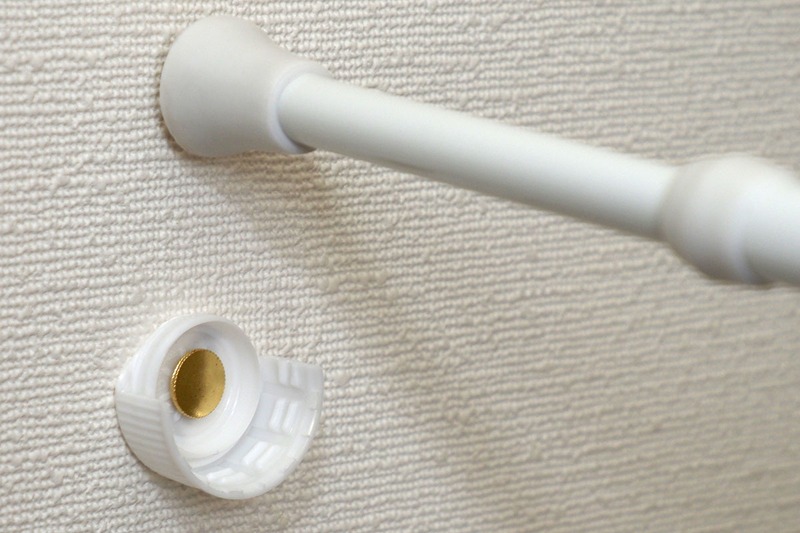 写真のように壁に固定して突っ張り棒を押し当てます。これで突っ張り棒がズリッと滑り落ちることが激減。壁に開く穴もあまり目立ちません。ただしペットボトルキャップや画鋲の固定力・保持力を上回る負荷がかかればズリッとイキますので、過信は禁物です。また、もちろんですが、この方法を使った場合も、突っ張り棒がなるべく強く突っ張るように固定してください。