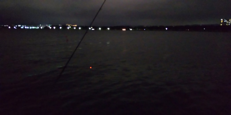 夜釣りの風景を撮影した3枚。周りに明かりがほとんどない、本当に暗い場所。手前に釣り竿、電気ウキが海面に浮かび、遠くに街の明かり。フラッシュオフ（左）、ライトオン（中）、フラッシュオン（右）。これはライトが一番良いと思うのですが