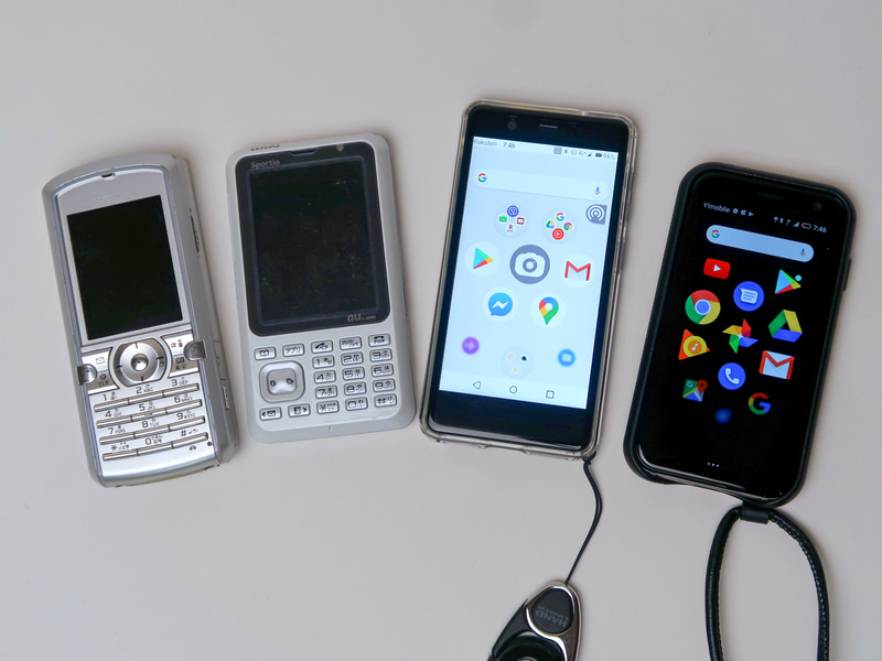 歴代の小型端末とRakuten Mini（右から2つ目）。ストラップホールが突いていて、ネックストラップを着ければ首から提げられる。透明のケースは楽天モバイル恵比寿店で購入した
