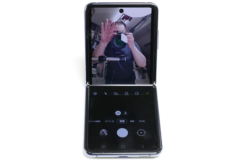 Galaxy Z Flipを置いてインカメラで自撮り。Galaxy Z Flipで自撮りする場合、手のひらをカメラに見せるとタイマーモードでシャッターが切れる（手のひらを引っ込める時間がある）。標準と広角の撮影モードがあり、自撮りに便利で、さらに机上などに置けるので自然な姿勢で自撮りできるというわけだ。