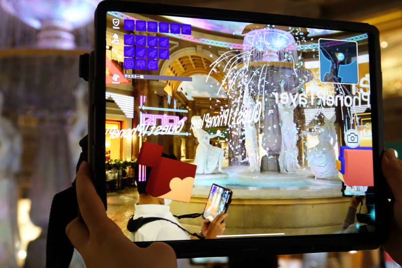 噴水周辺をiPadの画面を通して見た様子。仮想空間ならではの装飾が楽しめるほか、人物は自動的にアイコンになる