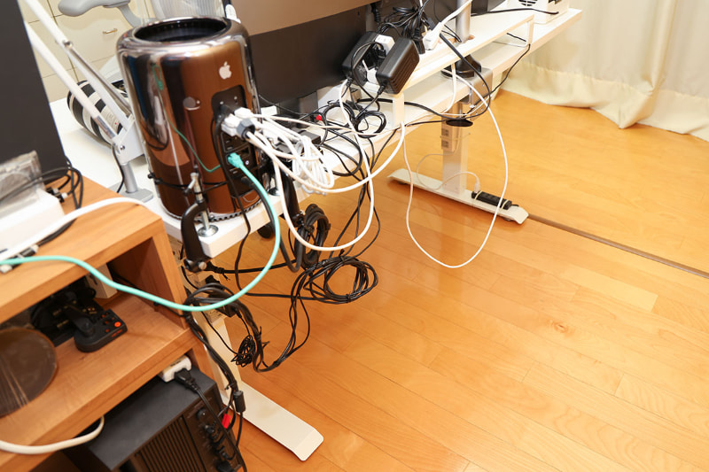 昇降デスクの背面。コンピュータを中心に配線がごちゃごちゃしているように見えるが……。じつは床にケーブルが着いていない。昇降デスク上のモノから伸びるケーブルが床に着いていると、昇降時にそのケーブルが床付近の何かに引っかかる可能性を拭いきれない。ケーブルが昇降デスク以外に触れていなければ、昇降時にそのケーブルが原因でトラブルが起きることは考えにくい、というわけだ