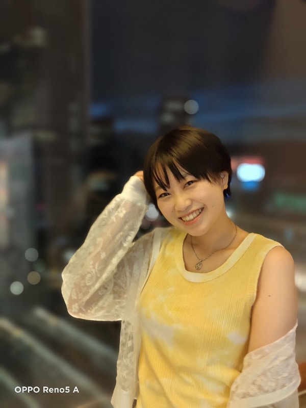 室内で夜景をバックに「ネオンポートレート」で撮影。人物を際立たせつつ、背景のライトが球状にボケている