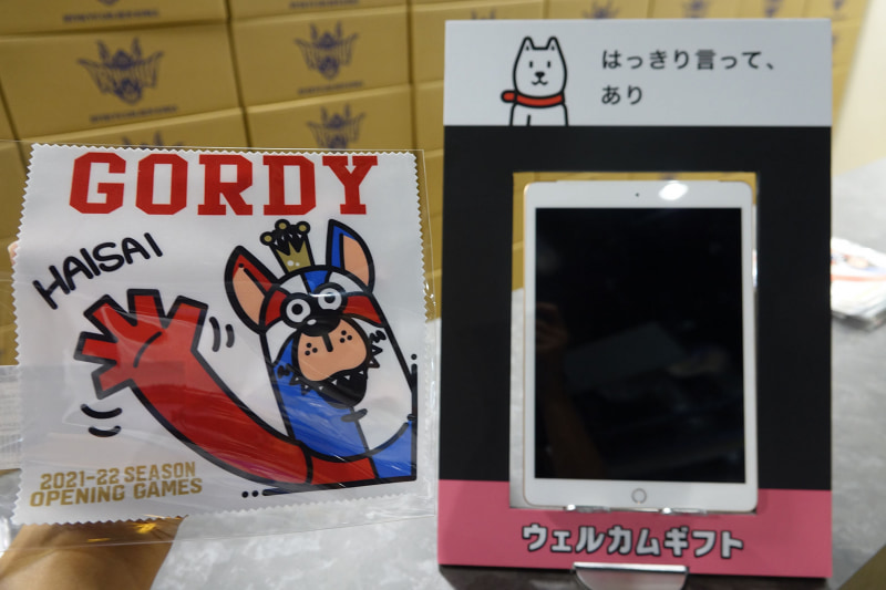 顔認証デバイスと配布されるオリジナルグッズ。グッズに描かれているのは、琉球ゴールデンキングスのマスコットキャラクター「ゴーディ」