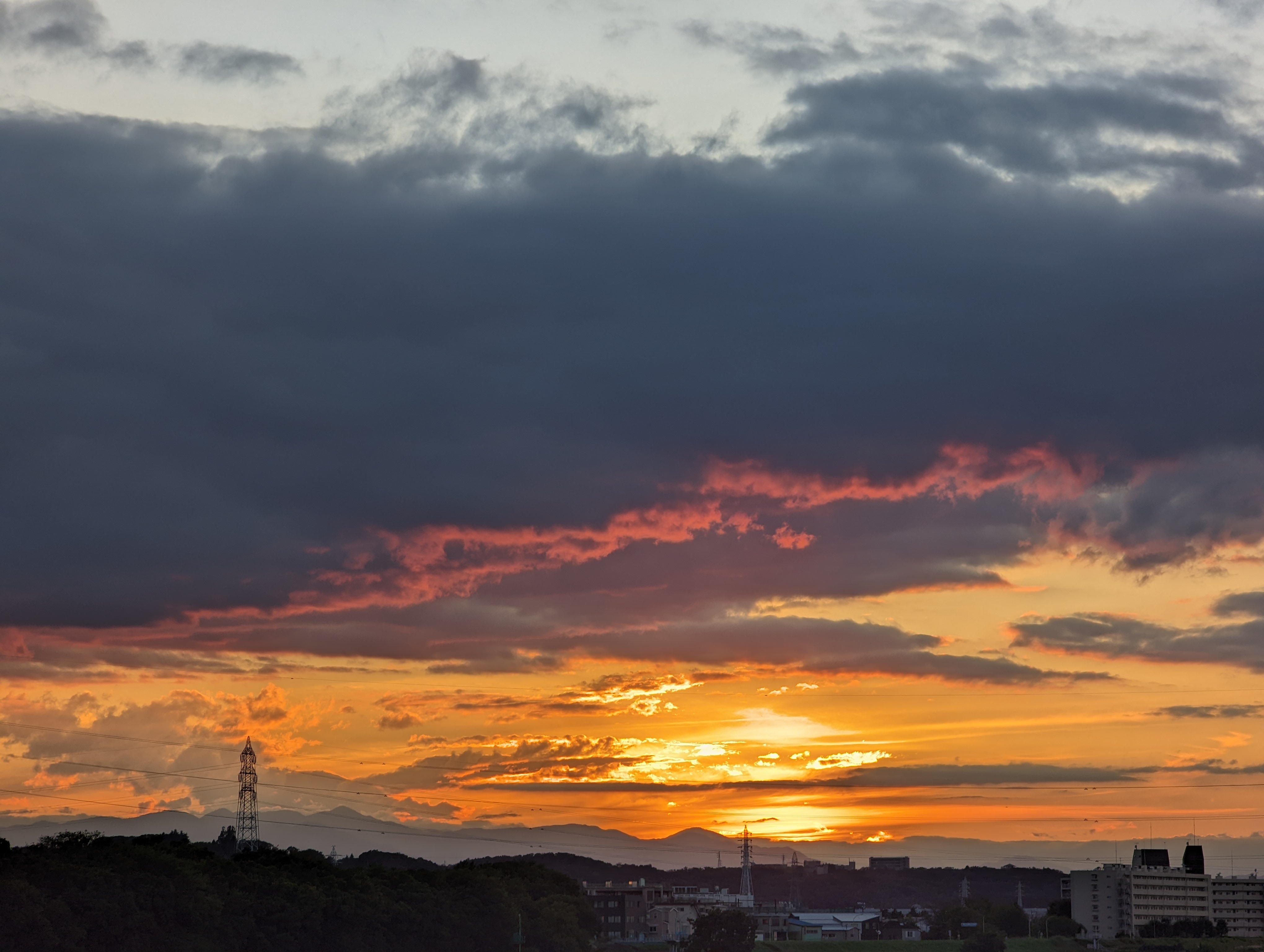 多摩川土手から丹沢の向こうに沈む夕日を望遠カメラで。太陽の左の山は大室山か。光源を真っ正面に捉えると、半円状のゴーストが上下に現れたが、オフセットすればクリーンな絵を手にすることが可能だ