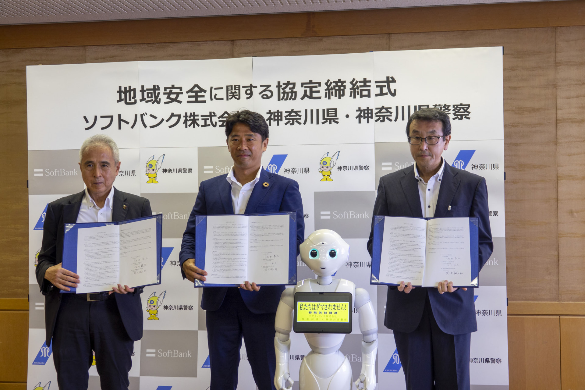 締結式のようす。左から神奈川県くらし安全防災局長の佐川 範久氏、ソフトバンクCSR本部長の池田昌人氏、ソフトバンクのロボット「Pepper」、神奈川県警察本部生活安全部長の則次 誠二郎氏