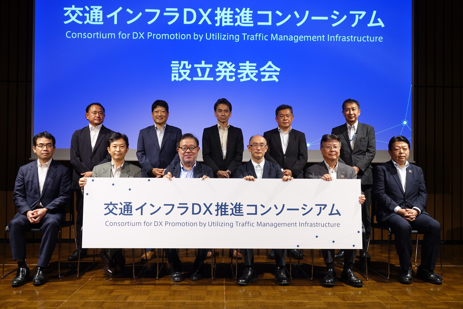 前列左から、JTOWER 田中敦史氏、慶應義塾大学 植原啓介氏、同 村井純氏、東京大学 大口敬氏、日本信号 流郷一宏氏、NEC 受川裕氏。後列左からNEC 長谷川隆氏、住友商事 梅田礼三氏、NEC 早川晶氏、本田技研工業 髙石秀明氏、住友電気工業 石丸弘之氏