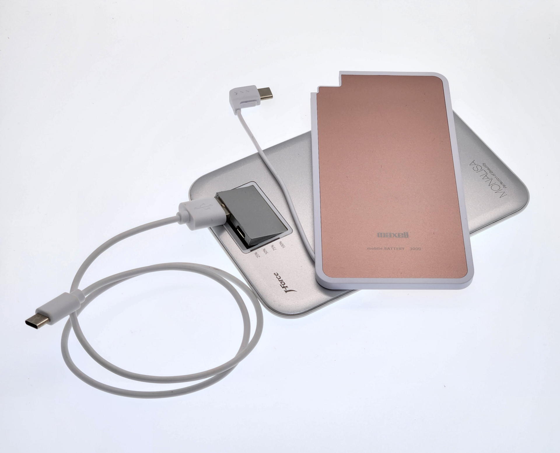 ギミックが筆者好みで普段から愛用しているフォースメディアのMONALISA（銀色、3400mAh、ケーブル込み実測127g）の方が薄く見えるが、実はマクセルのモバイルバッテリー（ピンク）の方が1㎜も薄い。なおかつUSBケーブルは内蔵式だ。買わない理由が見当たらない