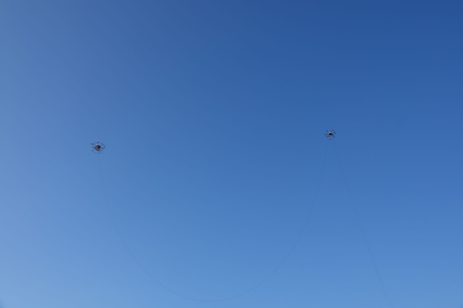 地上からのケーブルが、中継ドローンを介して基地局ドローンにつながっている