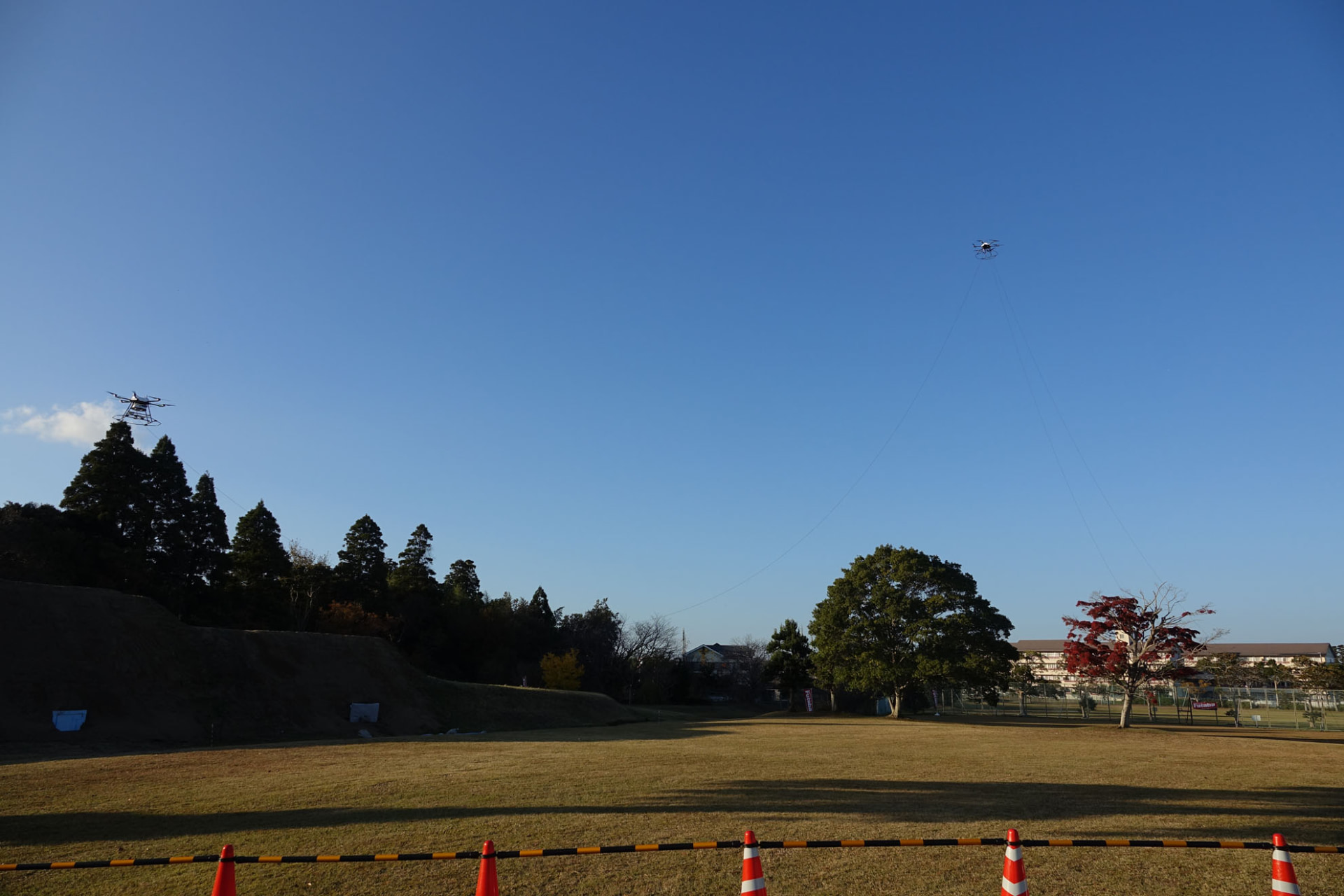 地上からのケーブルが、中継ドローンを介して基地局ドローンにつながっている