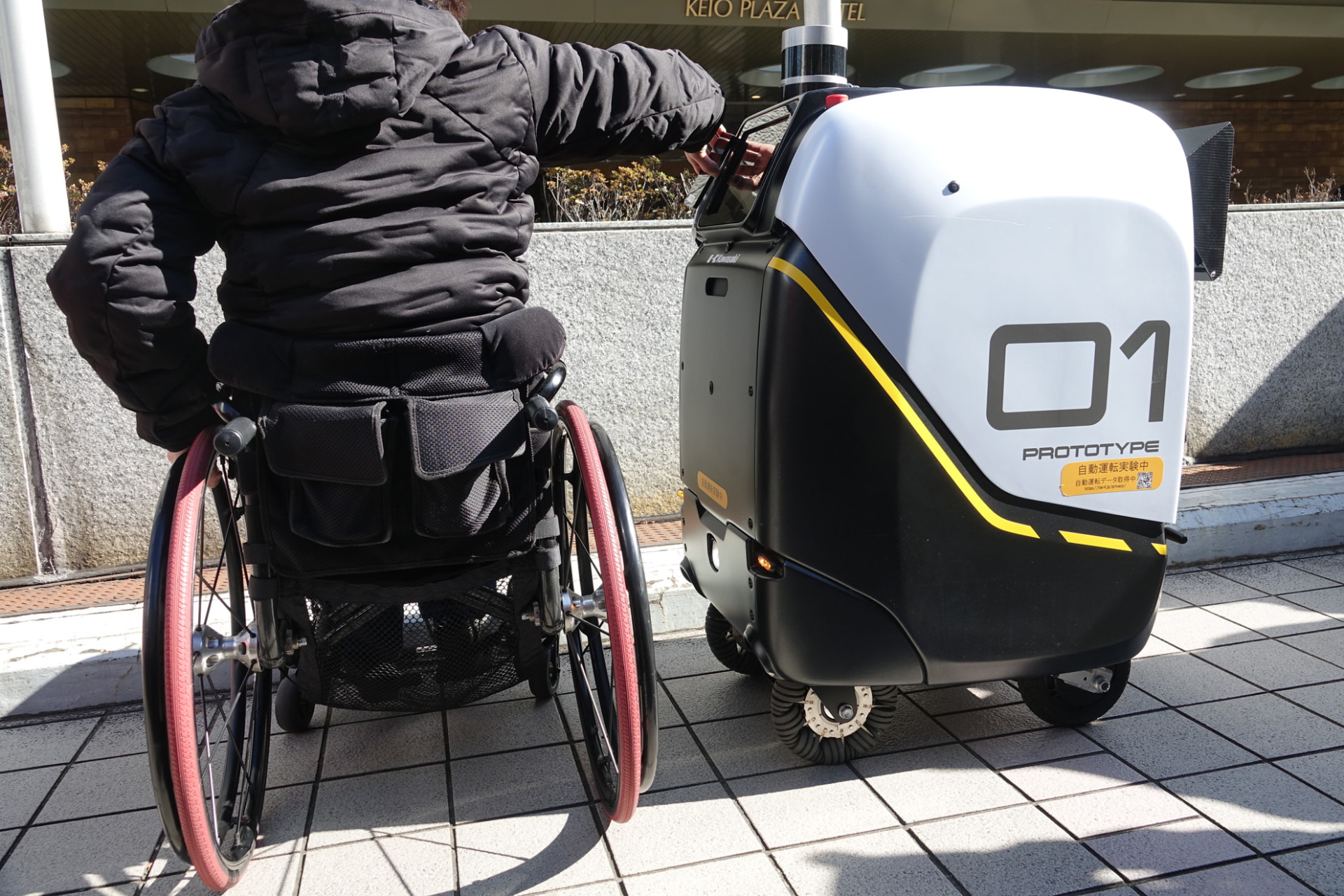 患者が荷物を受け取る。荷台のカバーは二次元コードを読み取らせると自動開閉する