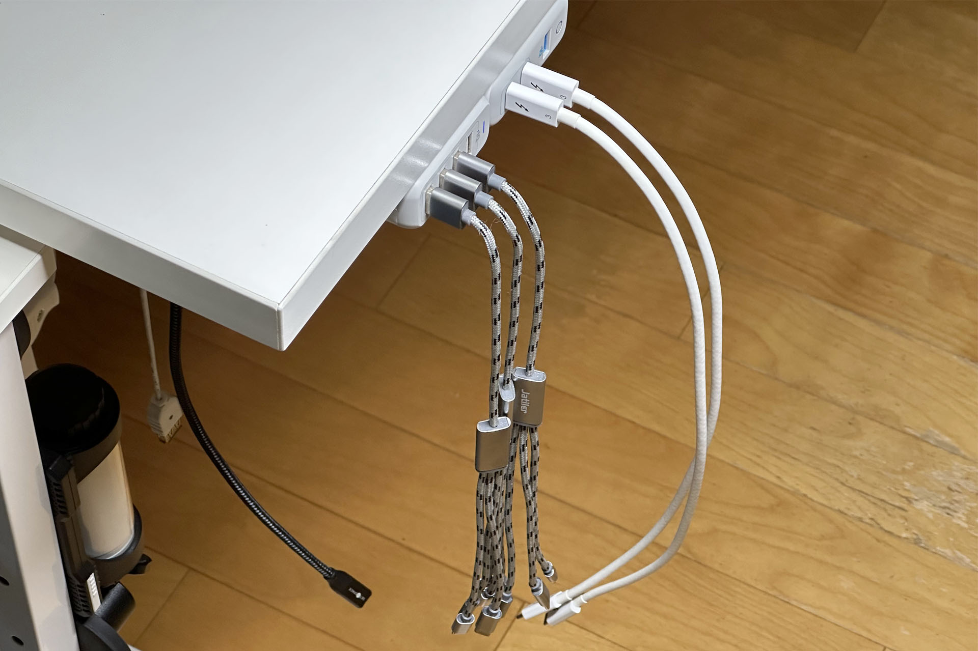 怪しい3つ又USBケーブル（手前）×3本と、マトモなUSB-Cケーブル×2本をつるしっぱなしにしている。ケーブルは床から20cmくらい上空までしか届かない短いタイプ。「不意にケーブルになにかをぶつけちゃうかな？」と思ったが、この2年で1度もぶつけたことがない