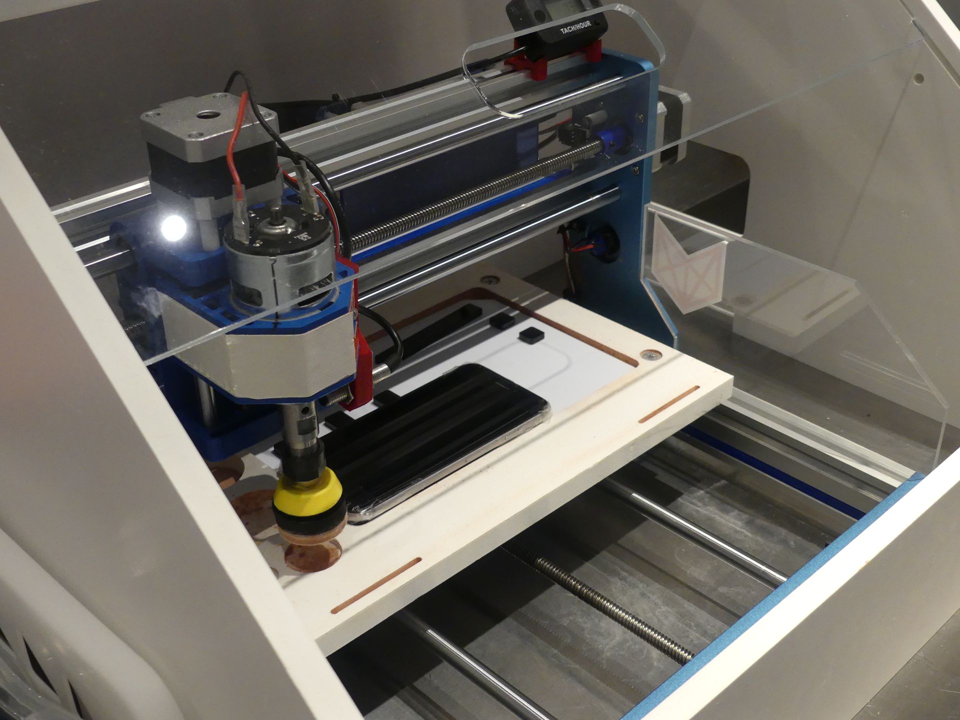 スマホ・スマートウォッチクリーニングの機械。ヘッドの先端にクッション性のあるパッドが装着されていて、それが高速に回転して画面を磨く（写真は端末が仮置きされた状態）