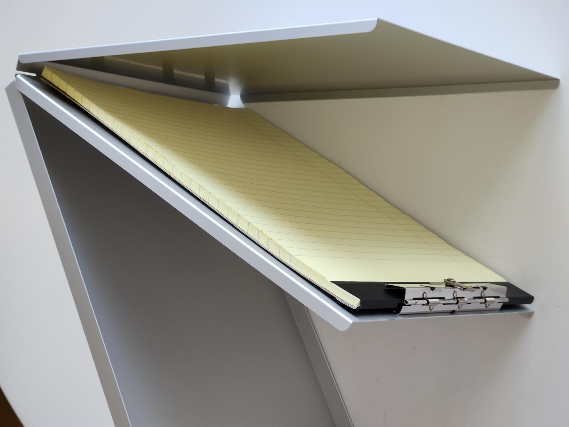 3枚のアルミ板を折り曲げてA4サイズ大のクリップボードと収納スペースを実現。収納スペースにはステーショナリー以外にも様々なモノを収納できる