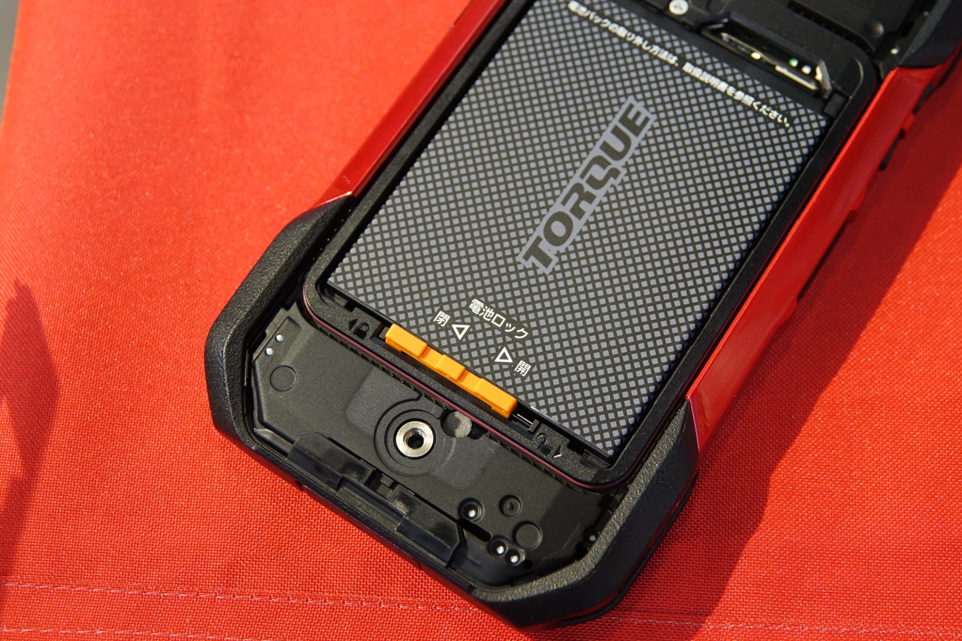 背面カバーは、下部のネジを回すことでロックが解除されるしくみ。先代モデルでは、90度回転させるだけでロック解除できたが、「小さい子供が誤って開けてしまうのを防ぐ」（担当者）などのため、今回はネジ式を採用している。ネジはコインなどを使って回せる