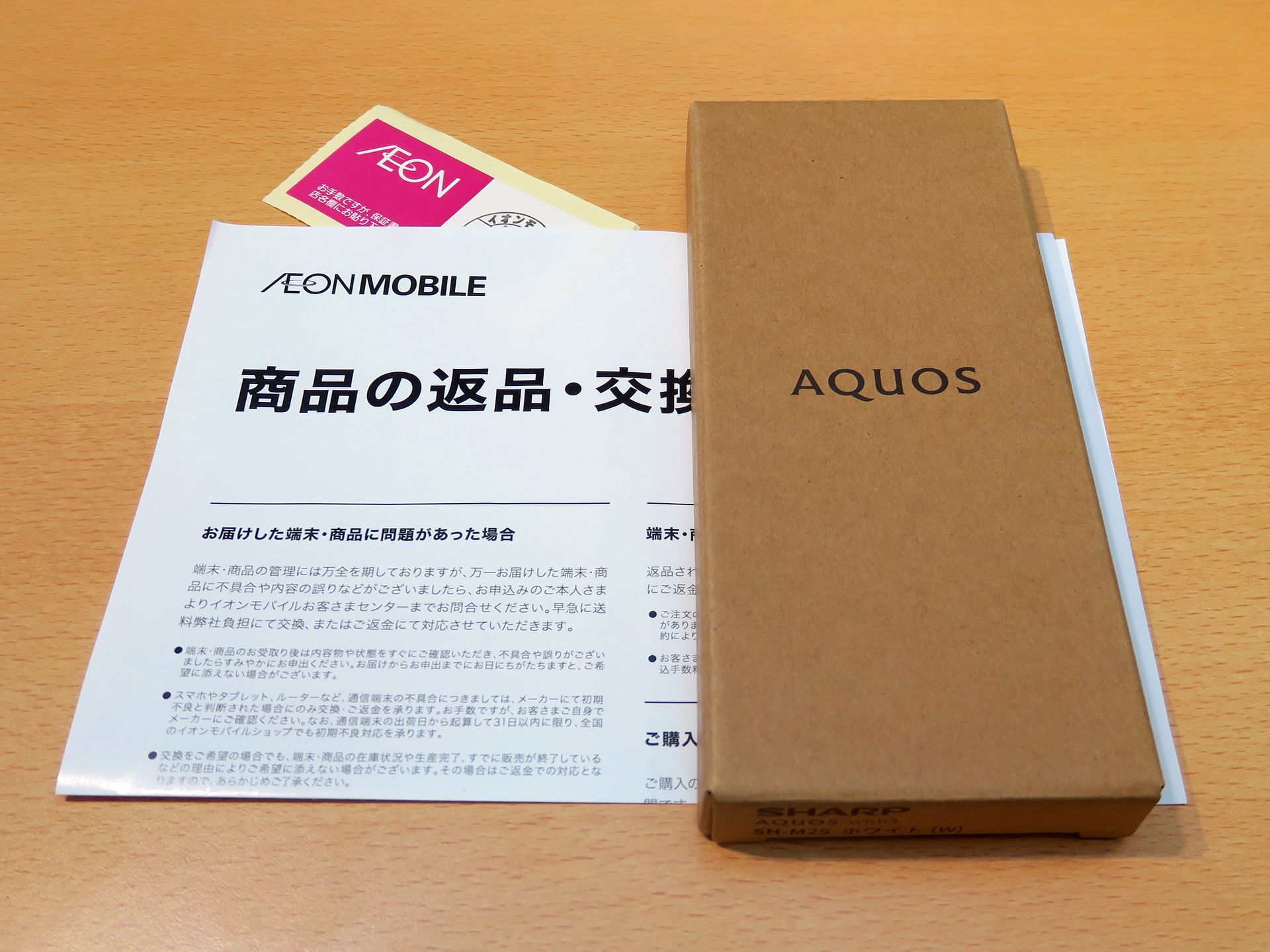 イオンモバイルから送られてきた「AQUOS wish3」には、「商品の返品と交換について」という紙と端末購入の保証シール（左上）のみ。保証シールは緩衝材の中に埋もれていたものが床に落ちて、発見できたけど……