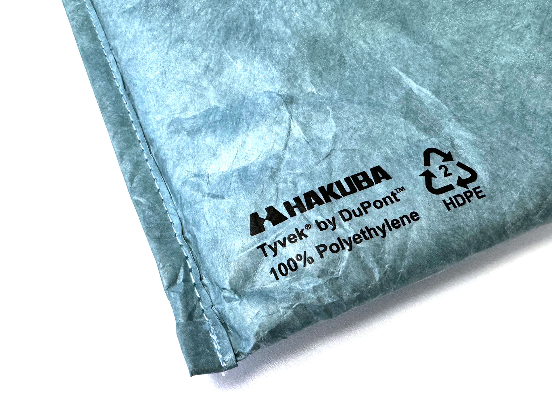 素材はデュポンの高密度ポリエチレン繊維不織布ことタイベック（Tyvek。強靱で耐久性があり、耐水性や透湿性・通気性があり、建材から服までいろいろな用途で使われている。紙のような質感で印刷なども可能だが、使っているとシワが出たり毛羽立ったりもしてくる。しかし耐久性が高いので、そうそう破れたりはしない。