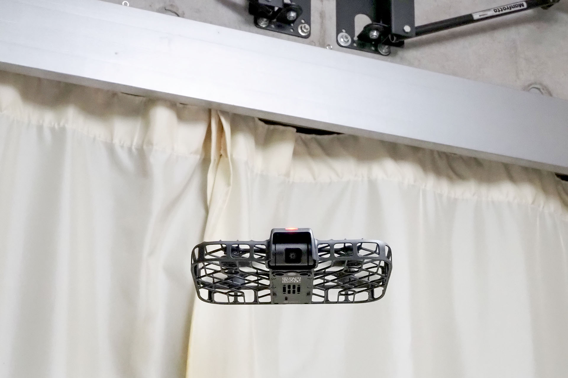 「HOVERAir X1 Smart」は、こんな感じでフツーの家の室内でも飛ばせる。限定的な使い方にはなるものの、けっこー楽しめる。空間に余裕があるオフィスなどならさらに楽しめるし、広さも高さもあるスタジオ的な施設ならも～っと楽しめるだろう。ちなみに、赤く見えるのは録画中を示すLEDランプで、その下にあるジンバルカメラはコチラ（顔）をターゲットとしてロックしている。